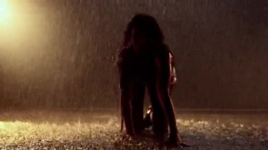 Bir dansçı yağmurda saçlarını kamçılıyor, hareketli turuncu ışıkla aydınlatılıyor ve büyüleyici bir görsel etki yaratıyor.