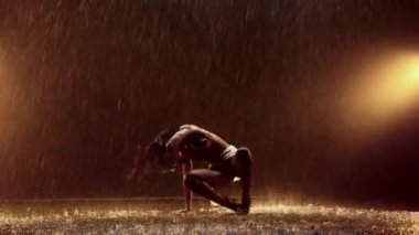 Bir dansçı, yağmurda büyüleyici bir performans sergileyerek hareketlerinin büyülü atmosferini arttıran çarpıcı su sıçramaları yaratır.