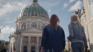 İki kadın yan yana Frederik 'in Kilisesi' ne doğru yürüyorlar. Sırtları kameraya dönük. Önlerinde muhteşem kilise kubbesi var.