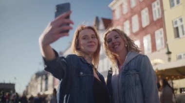 İki turist Nyhavn 'ın sembolik binalarının önünde selfie çekiyorlar. Canlı, tarihi arkaplana karşı neşeli anlarını yakalıyorlar.