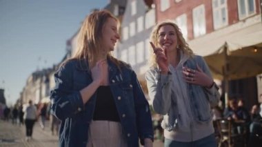 Nyhavn, Kopenhag 'ın canlı sokaklarında yürüyen iki turist, canlı atmosferin tadını çıkarıyor ve tarihi binalara hayran kalıyor.
