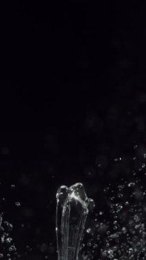 Çarpıcı bir yavaş çekim videosu, hareketli suyun güzelliğini ve akışkanlığını gözler önüne sererek, dinamik su sıçramaları yakalar ve siyah bir zemine doğru püskürtür.