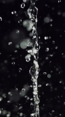Büyüleyici, yavaş çekim bir video kristal berrak su sergiliyor dramatik bir siyah arkaplan karşısında, her damlanın karmaşık güzelliğini ve akıcılığını vurguluyor.