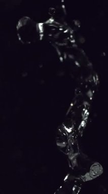 In a dark environment, a clear splash of water descends slowly, captured in fine detail as it falls