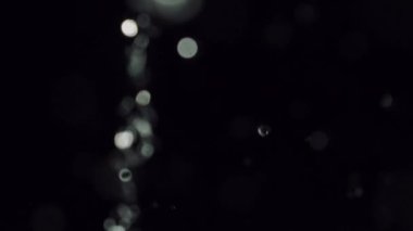 Karanlıkta su sıçratan büyüleyici bir yakın çekim. Titreyen bokeh parçacıkları ruhani bir parıltı yaratıyor.