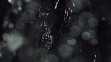 Büyüleyici bir yakın plan su, karanlık bir arkaplana sıçrıyor, titreyen bokeh parçacıkları dinamik ve büyüleyici bir etki yaratıyor.