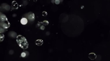 Bokeh parçacıklarının büyüleyici bir görüntüsü, zifiri karanlıkta berrak su damlacıklarının üzerinde parıldıyor.
