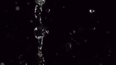 Karanlık bir arkaplanda parlayan parlak bokeh parçacıkları ve temiz su damlacıklarının büyüleyici bir görüntüsü rüya gibi ve büyüleyici bir ortam yaratıyor.