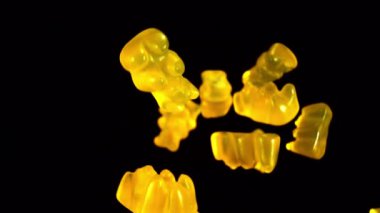 Sarı jelibon ayılar yavaş çekimde karanlık bir arkaplana karşı yüzerek büyüleyici bir renk ve hareket görüntüsü yaratırlar.