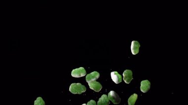 Şeker kaplı yeşil jelibonlar siyah bir arkaplan üzerinde yavaşça yüzerek büyüleyici bir renk ve doku görüntüsü oluştururlar.