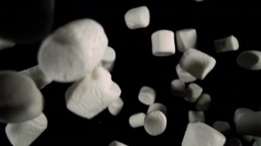 Beyaz marşmelovlar, yumuşak ve büyüleyici bir kontrastla yumuşak dokularını ön plana çıkaran koyu bir arkaplana doğru nazikçe süzülür ve düşerler.