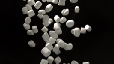 Yumuşak beyaz marşmelovlar yavaş çekimde koyu bir arkaplana doğru düşerek yumuşak dokular ve dinamik hareketin büyüleyici bir görüntüsünü oluşturur.