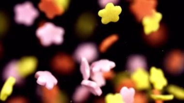 Renkli çiçekler kıvrılır ve karanlık bir arka plana doğru sürüklenir, rüya etkisi yaratmak için yumuşak bir odak ile yakalanır.