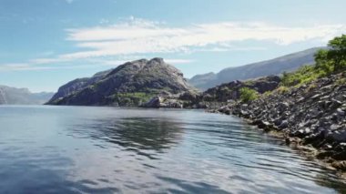 Engebeli bir kıyı şeridi üzerinde insansız hava aracı uçuşu, kıyı suları ve kayalık kıyılar, engebeli dağlar mavi gökyüzünün altında yükseliyor.