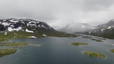 Uzak dağlardan çekilen çarpıcı bir hava görüntüsü yüzeyine dağılmış küçük adacıkları olan engin bir gölü ortaya çıkarıyor.