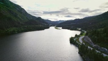 Bereketli yeşil dağlar arasında kıvrımlı bir nehir akıyor, yanında manzaralı bir yol var.