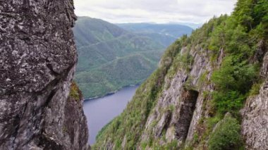 Geri çekilen bir çekim, yemyeşil dağlara bakan engebeli kayalıkları ve aşağıdaki nehri yakalar.