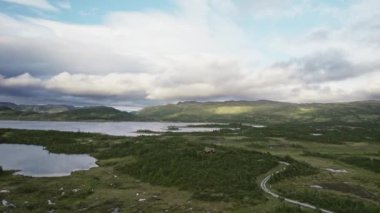 İnsansız hava aracı sakin yeşil bir arazide süzülüyor. Uzak evlerle kaplı. Kırsal kesimde yaşamanın barışçıl cazibesini sergiliyor.