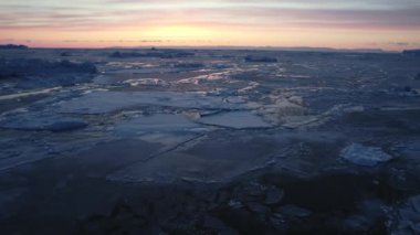 Günbatımı gökyüzü engin bir buz sahasının üzerine çarpıcı bir zemin çiziyor. Ufuk çizgisine kadar uzanıyor ve büyüleyici manzaranın dramatik bir görüntüsünü yaratıyor.