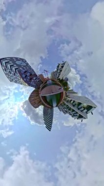 Büyüleyici küçük bir gezegen manzarası kentsel binalarla çevrili, değişen bulutları ve hareketli şehir yaşamını gösteren dinamik bir zaman dilimi ile güçlendirilmiş hareketli bir sahil yürüyüşü.