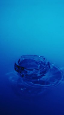 Sakinleştirici bir su damlası zarif bir şekilde sakin mavi bir yüzeye düşer ve sakin sahneyi canlandıran hafif dalgalanmalar yaratır.