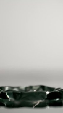 Tek bir su damlası, suyun saflığını ve berraklığını vurgulayarak, saf beyaz bir zemine doğru yavaşça iner.