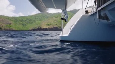 Bereketli yeşil bir dağın yanında seyir eden bir tekne, gövdenin bir kısmını gösteriyor ve altında sakin bir su, güneş ışığını yansıtan hafif dalgalar, bir huzur ve macera hissi uyandırıyor.