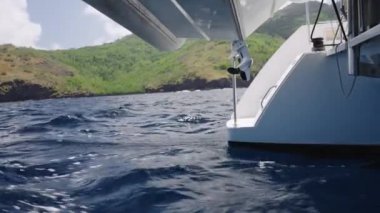 Açık bir gökyüzünün altındaki yemyeşil, dağlık kıyı şeridine karşı nazik dalgaları kesen gövdesiyle okyanusta seyreden bir tekne, denizdeki huzurlu bir macera duygusunu anımsatıyor.