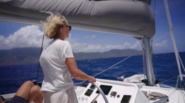 Bir arka plan görüntüsü, parlak, güneşli bir günde tekneyi süren bir kadını, dalgalı sarı saçları rüzgarda savrulurken, bir adamın bacağı onun ve teknenin kontrol panelinin yanında görünür bir şekilde yakalar.