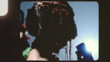 Büyüleyici bir sanatçı karmaşık bir başlık sergiliyor. Parlak stüdyo ışıklarına karşı poz veriyor.