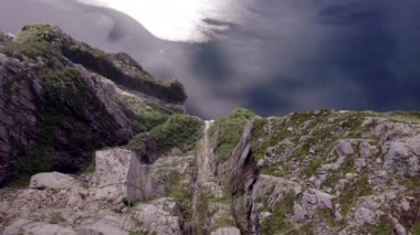 Kürsü Kayası 'nın üzerine çarpıcı bir dron inişi engebeli uçurum ile Lysefjorden' ın parıldayan yüzeyi arasındaki şaşırtıcı kontrastı gözler önüne seriyor, doğal güzellik ve sükuneti yakalıyor.