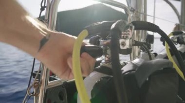 Yakın çekim, elinde dövmesi olan bir kişinin, bir tüpün kapakçığını ayarladığını, sakin bir arka plan ve uzak tepelere karşı durduğunu gösteriyor.