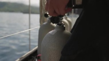 Bu yakın planda bir el, metal kopçalı bir kayışla bağlanmış metal bir valf ile bir dalış tüpünü ayarlar ve emniyete alır.