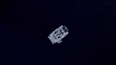 Çarpıcı bir manzara, bir yelkenliyi alçalan drone perspektifinden yakalar, ağırlıklı olarak beyaz gövdesini ve güneş panelleriyle donatılmış geniş güvertesini gösterir, bu arada uzun direkte tüylü yelkenli yelkenler bulunur.