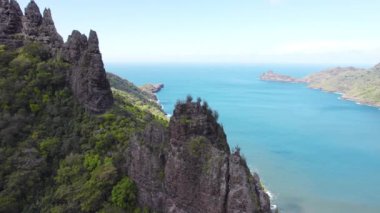 Hatiheus kayalık tepesi ve yemyeşil dağların üzerinde insansız hava aracı uçuşu, mavi okyanus ufkunun arka planına karşı canlı yeşil manzarayı sergiliyor.