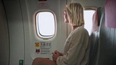 Pencere kenarında oturan bir kadın, uçak yolculuğu sırasında gökyüzünü izliyor.