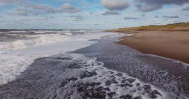 Huzurlu dalga desenleri Vesterhavet kıyısında zarifçe dalgalanır, dalgalar yumuşak kıvrımlı ibiklerle kıvrılarak narin deniz köpüğüne dönüşür.