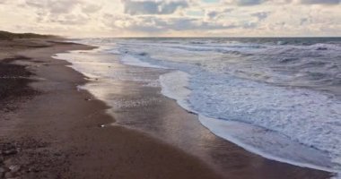 Vesterhavet 'in köpüklü dalgaları dinamik enerjiyle öne çıkar. Kıyı şeridi, geri çekilen suyun ardında karmaşık ve parıltılı desenler bırakmasıyla parlar.