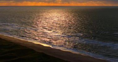 Altın bir günbatımı Vesterhavet 'in sakin dalgaları üzerinde hafifçe parıldıyor, sakin deniz manzarasının üzerine huzur verici bir parıltı saçıyor.