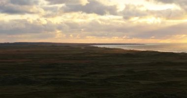 Huzurlu bir günbatımı yemyeşil tarlaların üzerine altın renkler saçar, Vesterhavet 'in yumuşak dalgaları dingin kıyı şeridini kaplar.