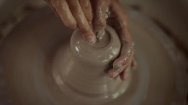 Dönen tekerlek üzerinde ustalıkla çömlek şekillendiren bir zanaatkârın yakın plan çekimi, balçığı eşsiz bir şekle dönüştürmenin ayrıntılı sürecine odaklanır.