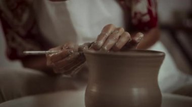 Çömlekçi çarkında hassas aletler olan bir zanaatkar çanak çömleği yakın plan, ayrıntılı el işçiliği ve ustalıklı el işi üzerine odaklanır
