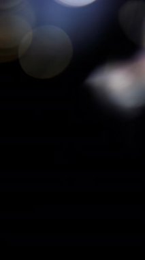 Yumuşak mavi ve beyaz bokeh küreleri yavaşça aşağı doğru hareket ediyor, karanlık, siyah bir zemin üzerinde, huzurlu ve ruhani bir atmosfer yaratıyor.