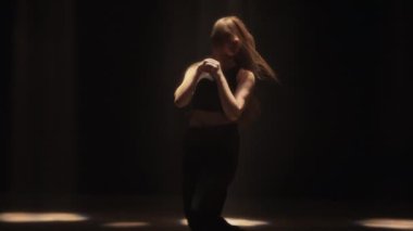 Serbest dans eden bir kız, keskin, akışkan hareketleri dramatik ışıklandırmayla vurgulanan loş bir odada dans eder.