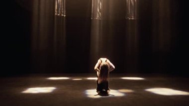 Loş bir stüdyoda, siyah elbiseli bir kız hareketlerinin ve hareketlerinin akıcılığını vurgulayan çağdaş bir dans sergiliyor.