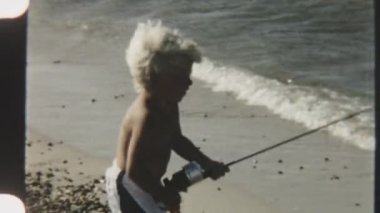 Genç bir çocuğun deniz kenarında oltasıyla sersemlemiş, okyanusun kenarında huzurlu bir gündüz vaktinin tadını çıkarırken çekilmiş klasik bir fotoğrafı.
