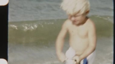 Plajda oltasını sallayan genç bir çocuğun arka planda hafif okyanus dalgaları sallanırken çekilmiş klasik görüntüsü.