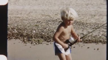 Bir çocuğun kumlu bir sahilde durup oltasını salladığı klasik bir fotoğraf.