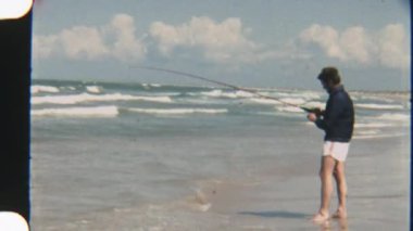 Bulutlu bir ufuk çizgisi ve arka planda dalgalanan dalgalarla balıkçı oltasını okyanusa atan bir adamın klasik çekimi.