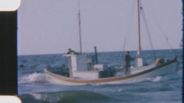 Balıkçılar kıyıya dönüyor, bir tanesi limana yanaşırken tekneye yardım ediyor, takım çalışmalarını ve kıyı balıkçılığı yaşam tarzını yakalıyor.